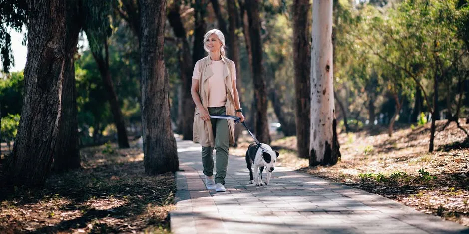 Mujer adulta paseando en medio de un parque en compañía de su mascota blanco con negro. Aprende cuánto vive un perro y disfruta más con él.