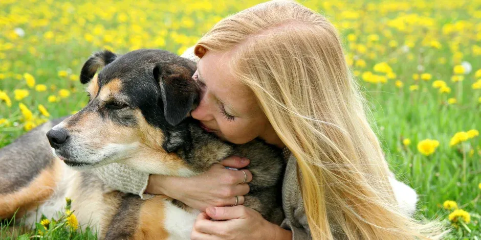 Mujer rubia que sabe cómo cuidar a un perro senior abrazando a su mascota.